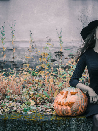 Happy creepy unrecognizible gothic young woman in witch halloween costume with halloween pumpkin.