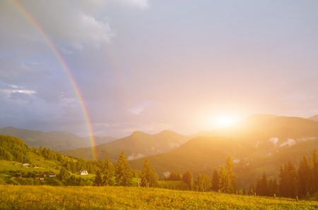 composite summer landscape. view from hillside to village near forest in high mountains in sunset lightの写真素材