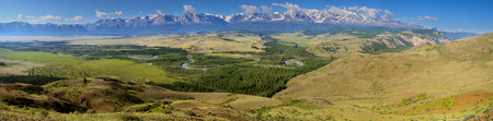 Over the mountain valley, snow-capped peaks in the clouds and green summer slopes, large panoramaの写真素材