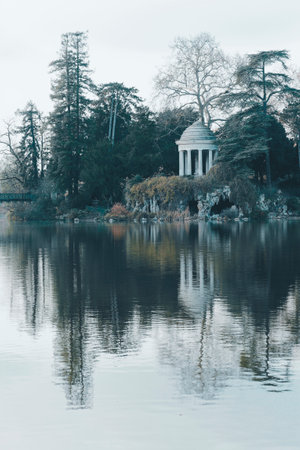 View of the rotunda and artificial grotto at ile de Reuilly on a calm day by Lake Daumesnil in Bois de Vincennes with tranquil water reflectionsの写真素材