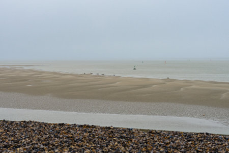 Coastal view at low tide with gray skies and distant boats in the waterの写真素材