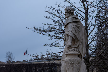 Statue of a historical figure under a cloudy sky near a building in an urban parkの写真素材