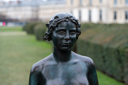 Bronze sculpture of a woman in an outdoor park surrounded by hedges and historical buildings during the dayの写真素材