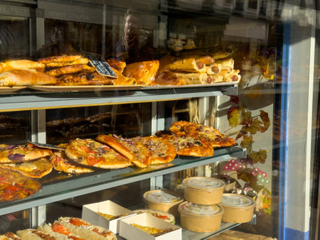 Freshly baked pastries and pizzas displayed in a bakery window during the morning hours in a lively urban settingの写真素材