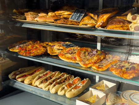 Wide variety of baked goods displayed in a bakery window during a sunny dayの写真素材
