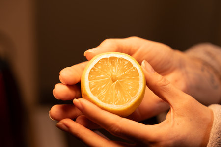 Slicing a fresh lemon held by hands in warm lighting creates a vibrant atmosphereの写真素材