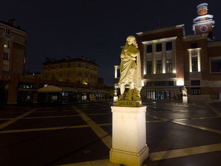 Statue of Moliere at night in a lively square surrounded by historic buildings and warm lightsの写真素材