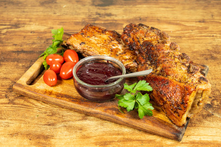 Deliciously grilled meat platter with fresh tomatoes and savory sauce on a wooden boardの写真素材