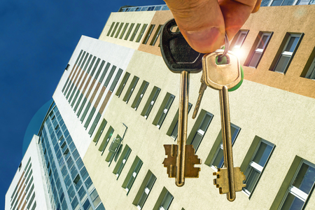 The keys to the apartment in the background of a new residential homes. The concept of changes in prices on the real estate marketの写真素材