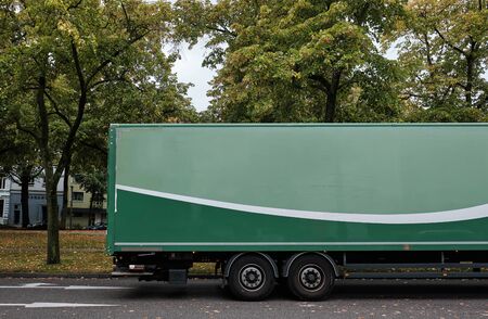 Side view of a green trailer with empty space for graphics in a road with green treesの写真素材