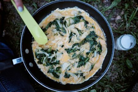 Top view of a woman cooking an omelette with spinach and onions using a camping fire 