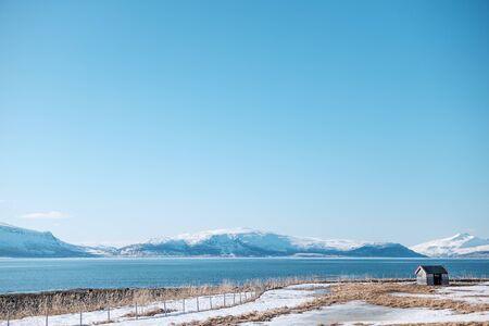 Tromso, Norway - April 29 2018: Isolated abandoned hut on fjord shore in a clear sunny day with...