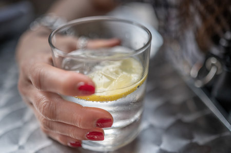 Close-up of a woman's hand holding a glass of water with lemonの写真素材