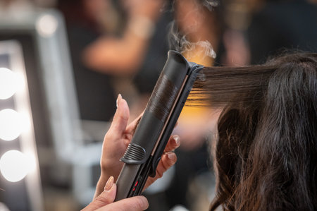 Professional hairdresser using curling iron to straighten hairの写真素材