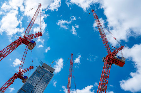 Construction cranes and building under construction against blue sky with white clouds