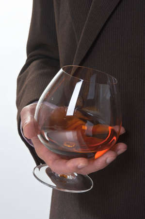Glass with alcohol in a hand of the man in a suit on a light background