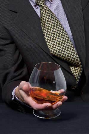 The man holds in a hand a glass with alcohol against a dark suitの写真素材