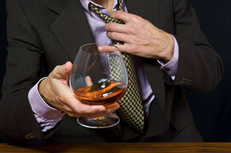 Glass with alcohol in a hand of the man in a suit on a light backgroundの写真素材