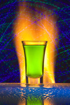 Glass with alcohol against fire with reflexion. Against a dark background with colour small lamps.の写真素材