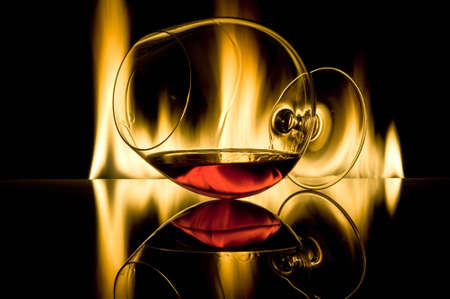 The glass with cognac lies horizontally against fire with reflexion against a dark backgroundの写真素材