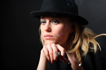 Portrait of the beautiful girl in a hat on a black background with a cigarの写真素材