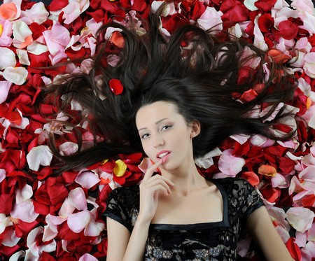 Portrait of beautiful brunette in red rose petalsの写真素材