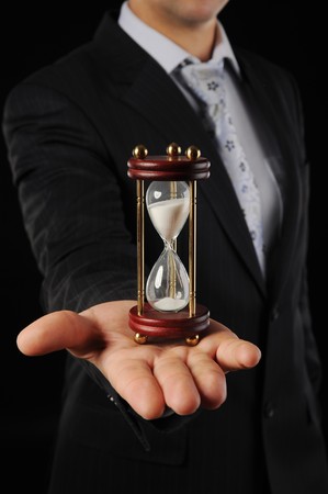 Businessman with hourglass in hand in a dark roomの写真素材