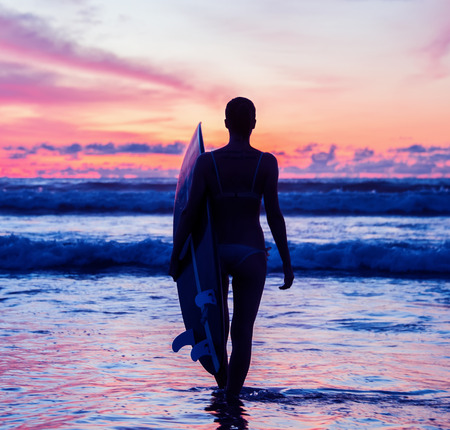 Beautiful young woman surfer with board on the beachの写真素材