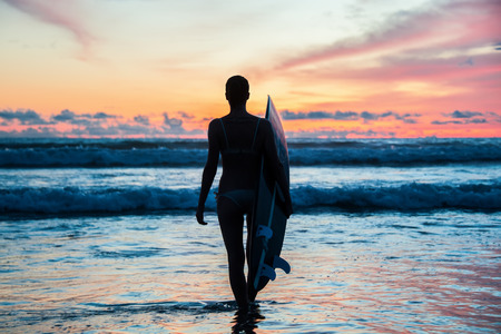 Beautiful young woman surfer with board on the beachの写真素材