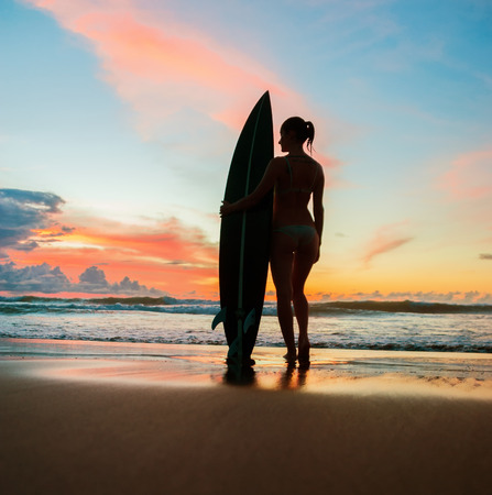 Beautiful young woman surfer with board on the beachの写真素材