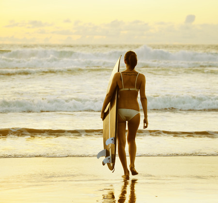 Beautiful young woman surfer with board on the beachの写真素材