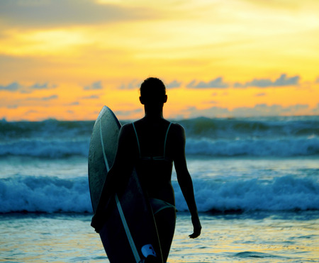 Beautiful young woman surfer with board on the beachの写真素材