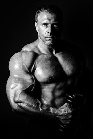 bodybuilder posing. Handsome power athletic guy male. Fitness muscular body on black background. Black and white photoの写真素材