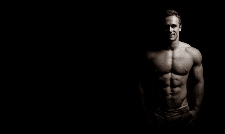 bodybuilder posing. Handsome power athletic guy male. Fitness muscular body on black background. Black and white photoの写真素材