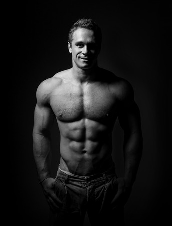 bodybuilder posing. Handsome power athletic guy male. Fitness muscular body on black background. Black and white photoの写真素材