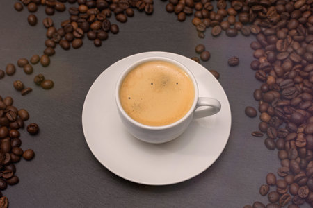 white cup with espresso coffee on a saucer with coffee beans on a dark background. High quality photoの写真素材