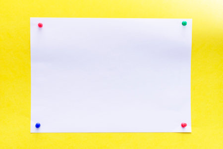 empty white sheet of paper pinned with push pins on a yellow background. High quality photoの写真素材