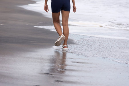 Legs of a girl in sandals walking alone along a sandy beach along the sea. High quality photoの写真素材