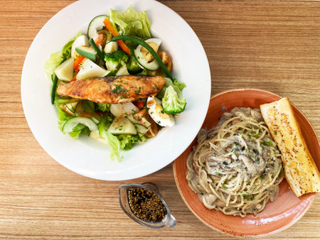 Pasta with mushrooms and a plate with a salad of vegetables and grilled salmon on a wooden background. High quality photoの写真素材