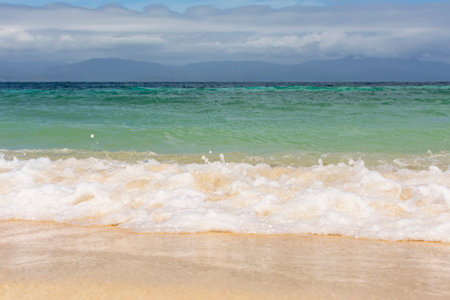 Soft wave on the beach with yellow sand against the backdrop of mountains and the sea. High quality photoの写真素材