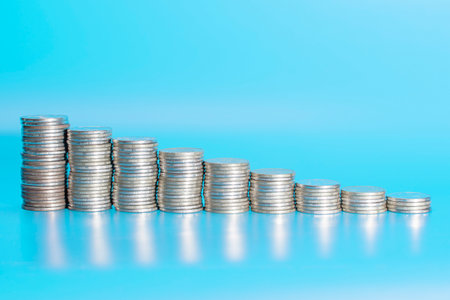 stacks of coins from largest to smallest on a blue background. decline in economy and income. High...