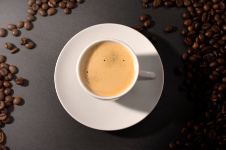 white cup with espresso coffee on a saucer with coffee beans on a dark background. High quality photoの写真素材