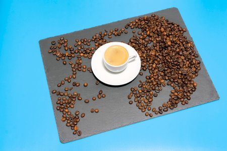 white cup with espresso coffee on a saucer with coffee beans on a dark and blue background. High quality photoの写真素材