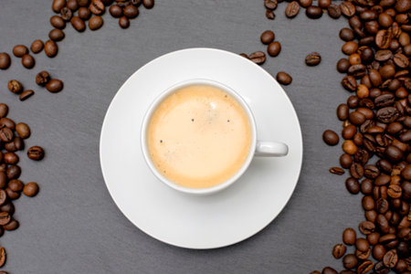 white cup with espresso coffee on a saucer with coffee beans on a dark background. High quality photoの写真素材