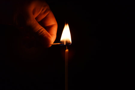 male hand lights a candle with a match on a black background. church candle. High quality photoの写真素材