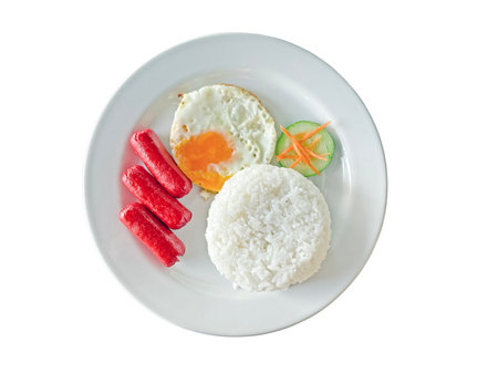Breakfast on a white plate including sausages, rice, fried egg, fresh vegetables isolated on peach background. High quality photoの写真素材