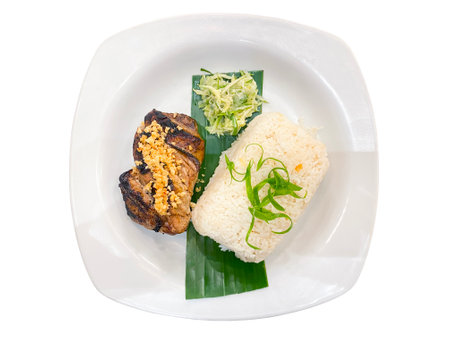 Grilled piece of tuna with rice and vegetable salad on a banana leaf on a white plate isolated on a white background.の写真素材