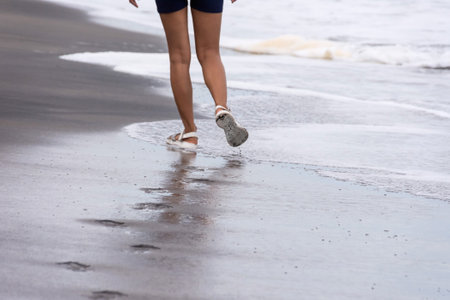 Legs of a girl in sandals walking alone along a sandy beach along the sea. High quality photoの写真素材