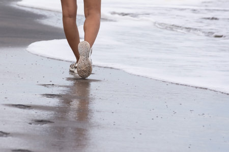 Legs of a girl in sandals walking alone along a sandy beach along the sea. High quality photoの写真素材