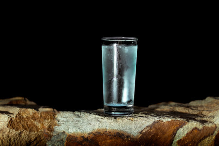 a glass of water with walls fogged up from the cold on a rock on a black background. High quality photoの写真素材
